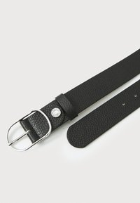 Svart lærbelte med strukturert finish, som har en spenne i sølvmetall og en trykknappdetalj med et merkenavn. Glatte kanter, justerbar lengde.
