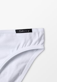 Culotte blanche en coton avec une texture lisse, dotée d'une étiquette noire avec le nom de la marque "Skiny" sur la taille. Design et forme simples.