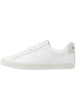 Baskets en cuir blanc avec une semelle en caoutchouc texturée et blanc cassé. Les caractéristiques incluent des lacets, des coutures discrètes et un accent en daim gris au niveau du talon.