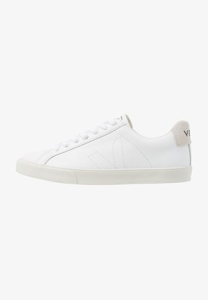 White leather sneakers with a textured off-white rubber sole. Features include laces, subtle stitching, and a grey suede heel accent.