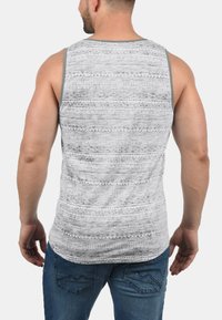 Grå og hvit mønstrete tank topp med en teksturert design, som har brede skulderstropper og grå kant. Brukt sammen med jeans.