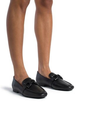Mocassins en cuir noir avec une finition lisse, dotés d'un détail de boucle décoratif, d'un bout arrondi et d'un faible talon, sur un fond blanc.
