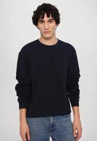 Sweatshirt azul-marinho com mangas longas, gola redonda e punhos canelados, combinado com jeans de denim azul. Tecido de algodão macio, corte casual.
