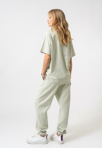 Mīlīgi zaļa kokvilnas-lina maisījuma T-krekls un atbilstoši joggeri. Brīva piegriezuma ar īsām piedurknēm, sānu kabatām un ribotām cuffs. Masīvas baltas sporta kurpes.