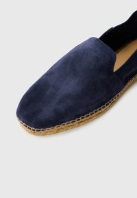 Espadrila od tamnoplave suede kože s prirodnom pletenom jute potplatom i dizajnom za lako navlačenje na bijeloj pozadini.