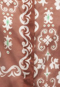 Καφέ ύφασμα με λευκά λουλουδάτα και διακοσμητικά σχέδια, τονισμένο με μικρές πράσινες κουκκίδες, με κεντρική κάθετη ραφή.