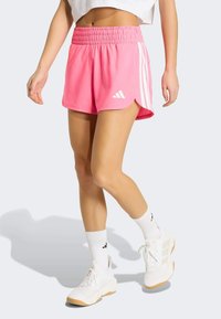Shorts de sport roses avec une taille élastique, trois bandes blanches sur les côtés et un logo blanc sur le devant.