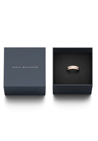 Vaaleanpunakulta- ja hopeasormus esillä tummansinisessä neliönmuotoisessa laatikossa, jossa on kultaiset kohokuvioidut logot. Musta pehmustettu sisustus suojaa sormusta.