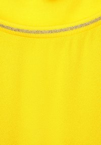 Žlutá látka s texturovaným povrchem a zaobleným výstřihem, doplněná stříbrnou ozdobou podél výstřihu.