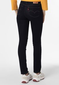 Jeans ajustados de mezclilla azul oscura con costuras amarillas en contraste, que presentan un diseño clásico de cinco bolsillos y un parche de cuero de marca en la parte trasera.