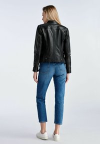 Czarna skórzana kurtka o dopasowanym kroju, do kolan, z teksturowanym wykończeniem. W połączeniu z niebieskimi dżinsami o prostych nogawkach i białymi trampkami.