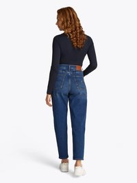 Augstās jostas daļas zilas denim bikses ar taisnām kājām, ar aizmugures kabatām un brūnu ādas etiķeti jostasvietā. Saskaņotas ar melnu garām piedurknēm topu un baltām sporta apaviem.
