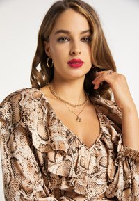 Lichtgewicht snakeprint blouse met ruches aan de mouwen, diep V-hals en een zachte textuur. Een gouden gelaagde ketting en oorringen accentueren het ontwerp.