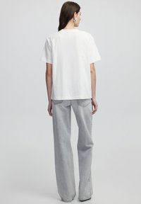 T-shirt en coton blanc avec une coupe décontractée, des manches courtes et un col rond, associé à un jean large gris clair avec des détails de poches.