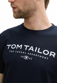T-Shirt aus Baumwolle in Marineblau mit Rundhalsausschnitt, mit weißem Text: "TOM TAILOR THE CASUAL DEPARTMENT 1962." Weicher Stoff, lässiges Design.