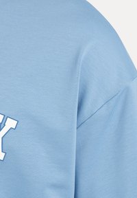 Helles blaues Baumwoll-T-Shirt mit strukturiertem Finish, ausgestattet mit einem großen weißen Druckbuchstaben-Design auf der Vorderseite und einer lockeren Passform.
