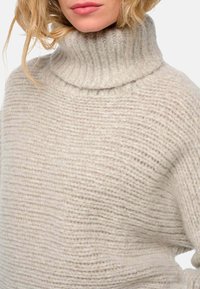 Beige Strickpullover mit hohem, geripptem Rollkragen. Verfügt über eine lockere Passform und eine strukturierte Oberfläche, die durchgehende horizontale Streifen zeigt.
