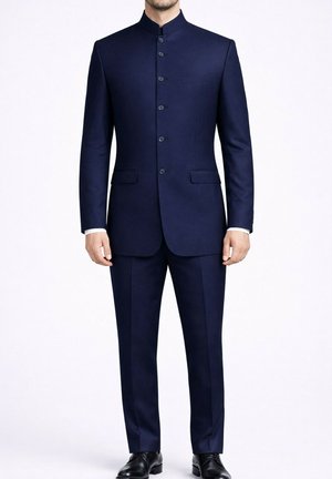 Homme portant un costume bleu marine sur mesure à col Nehru avec des chaussures habillées noires, debout devant un fond blanc uni.