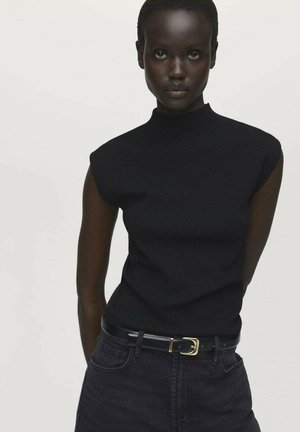 Haut sans manches en tricot noir côtelé avec un col montant, associé à un jean en denim foncé et une ceinture noire avec une boucle en or.