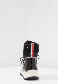 Czarny wodoodporny but z błyszczącym wykończeniem, futrzanym kołnierzem oraz detalem w paski w kolorach czerwonym, białym i niebieskim. Posiada okrągłe przelotki i masywną podeszwę.