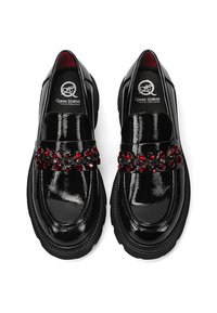 Černé lakované kožené mokasíny s hladkým povrchem, zdobené dekorativním pruhem červených a černých drahokamů. Gumičková podešev s texturovanými okraji.