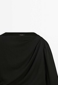 Black fabric top featuring a wide neckline, draped design, and softly structured sleeves. Tag visible at the neckline.