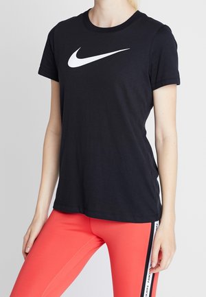 Osoba nosząca czarną koszulkę Nike z białym logo Swoosh oraz jaskrawoczerwone legginsy z bocznymi paskami z logo Nike.