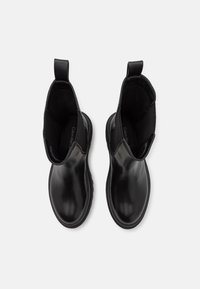 Paire de bottines Chelsea en cuir noir brillant avec panneaux latéraux élastiques et brides de traction, vues de dessus sur un fond blanc.