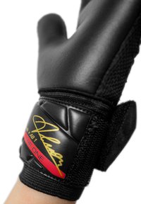 Black goalkeeper glove featuring textured latex palm, mesh finger design, and a Velcro wrist strap with a gold signature and red accents.