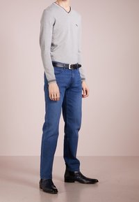 Hellgrauer V-Ausschnitt-Pullover, tailliert, mit schwarzem Rand; blaue gerade Jeans; schwarze Stiefel; minimale Details.