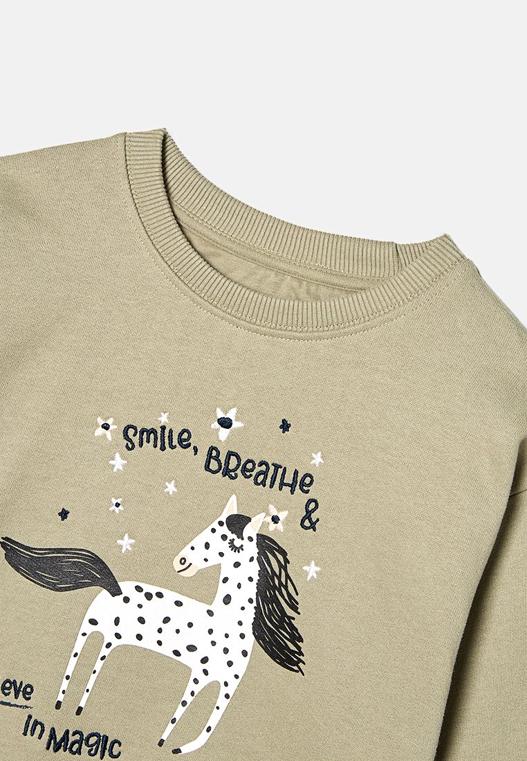 Hellolivgrüner Pullover mit einem weißen Pferde-Design, das schwarze Flecken und eine Mähne hat, umgeben von Text und Sternmotiven. Gerippter Halsausschnitt.