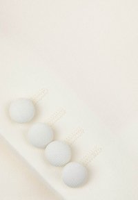 Biały materiał z czterema teksturowanymi guzikami w rzędzie. Guziki mają subtelny wzór i są przymocowane do materiału za pomocą dopasowanych uszek.