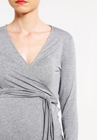 Grey long-sleeve wrap top in jersey fabric features a deep V-neckline and a knot detail at the waist, offering a fitted silhouette.