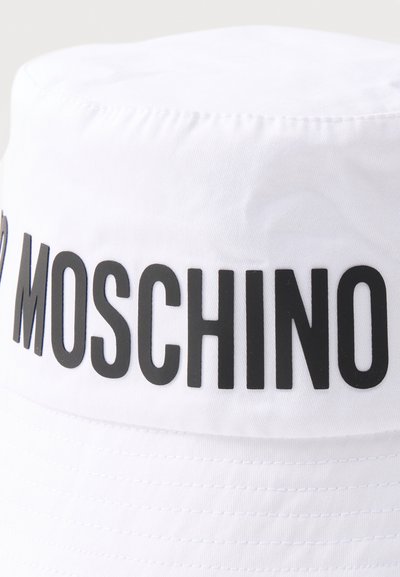 Λευκό υφασμάτινο καπέλο τύπου bucket με μεγάλα μαύρα γράμματα που σχηματίζουν τη λέξη «MOSCHINO» γύρω από την κορυφή.