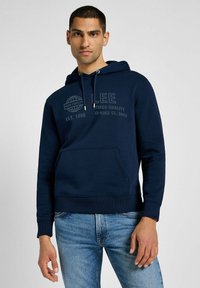 Granatowy hoodie z przednią kieszenią typu kangur, kapturem ze sznurkiem oraz nadrukowanym tekstem. Rybne mankiety i dół, wykonany z miękkiego materiału bawełnianego.