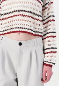 Crochet knit top with red, navy, and cream stripes, paired with high-waisted light gray trousers featuring a single black button.