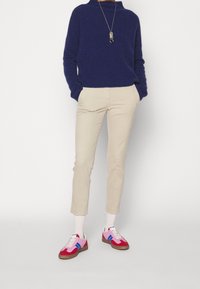 Marineblauer Pullover, beigen Hosen und bunten Sneakern mit pinken, blauen und weißen Akzenten. Weiße Socken sichtbar. Einfaches, lässiges Outfit.