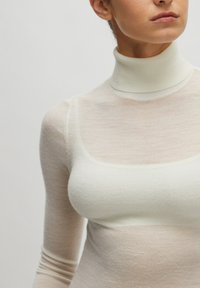 Leichtes Rollkragenoberteil in Creme mit geripptem Kragen und langen Ärmeln, versehen mit einer transparenten, strukturierten Überlage und quadratischem Ausschnitt.