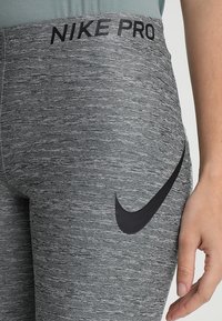 Leggings Nike Pro in grigio mélange con tessuto testurizzato, dotati di un logo nero all'anca e una cintura ampia con il marchio "NIKE PRO".