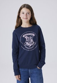Sweatshirt marine à manches longues, avec un graphique du blason de Poudlard en rose clair centré sur le devant et des poignets et un ourlet côtelés.