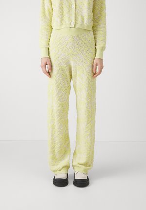 Ensemble de détente en tissu texturé jaune clair, comprenant un cardigan à motif et un pantalon assorti avec des poignets côtelés, complété par des chaussures noires.