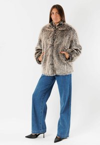 Cappotto in pelliccia sintetica in tonalità grigie con colletto alto e tasche laterali, abbinato a jeans in denim blu a gamba larga e décolleté nere a punta.