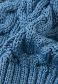 Jasnoniebieska dziana tkanina o teksturowanym wzorze, z zawijającymi się kablami i prążkowanymi sekcjami, wykonana z miękkiej, grubej włóczki.