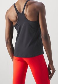 Czarny sportowy tank top z racerbackiem, zestawiony z jaskrawoczerwonymi legginsami. Gładka faktura, dopasowany krój i minimalistyczny styl.