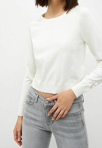 Biały sweter w prążki o okrągłym dekolcie i długich rękawach, zestawiony z szarymi dżinsami z zapięciem na guzik i przednimi kieszeniami.