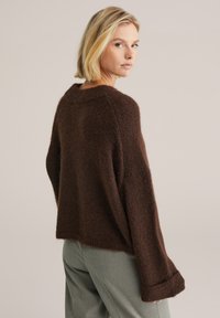 Pulover maro pufos cu o croială lejeră, mâneci largi și tiv nervurat. Textura moale sporește căldura; design minimalist, fără modele.