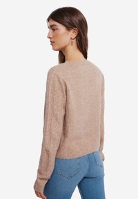 Beige gebreid sweater met ribbels en kabelgebreide mouwen. Het ontwerp is getailleerd en heeft een ronde halslijn, gedragen met een blauwe jeans.