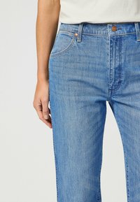 Vaqueros de denim de color azul claro con un diseño de pierna recta y textura sutil. Cuenta con herrajes en tono cobre y bolsillos frontales.
