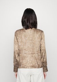 Chemise marron à manches longues avec un motif texturé de rayures verticales blanches. Présente des manches ajustées et une coupe droite, fabriquée à partir d'un matériau léger.