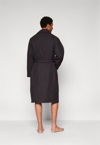 Waffle-textured, dark gray bathrobe with a belted waist and shawl collar, reaching mid-calf, designed for comfort and ease of movement.